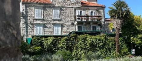 A stone building with a red-tiled roof, multiple windows, and a balcony.