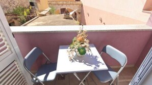 Un balcón con una mesa, dos sillas, una planta en maceta y vista a un edificio al fondo.
