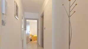 Un pasillo con una puerta al final que da a una habitación con cama y mesita de noche.