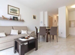 Sala de estar com sofá, mesa de centro e área de jantar com cadeiras.