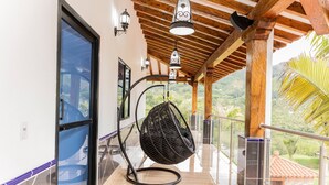 A balcony with a hanging chair, glass doors, and a view of greenery. - Ecohotel Dubai Del Oriente (El Penol)