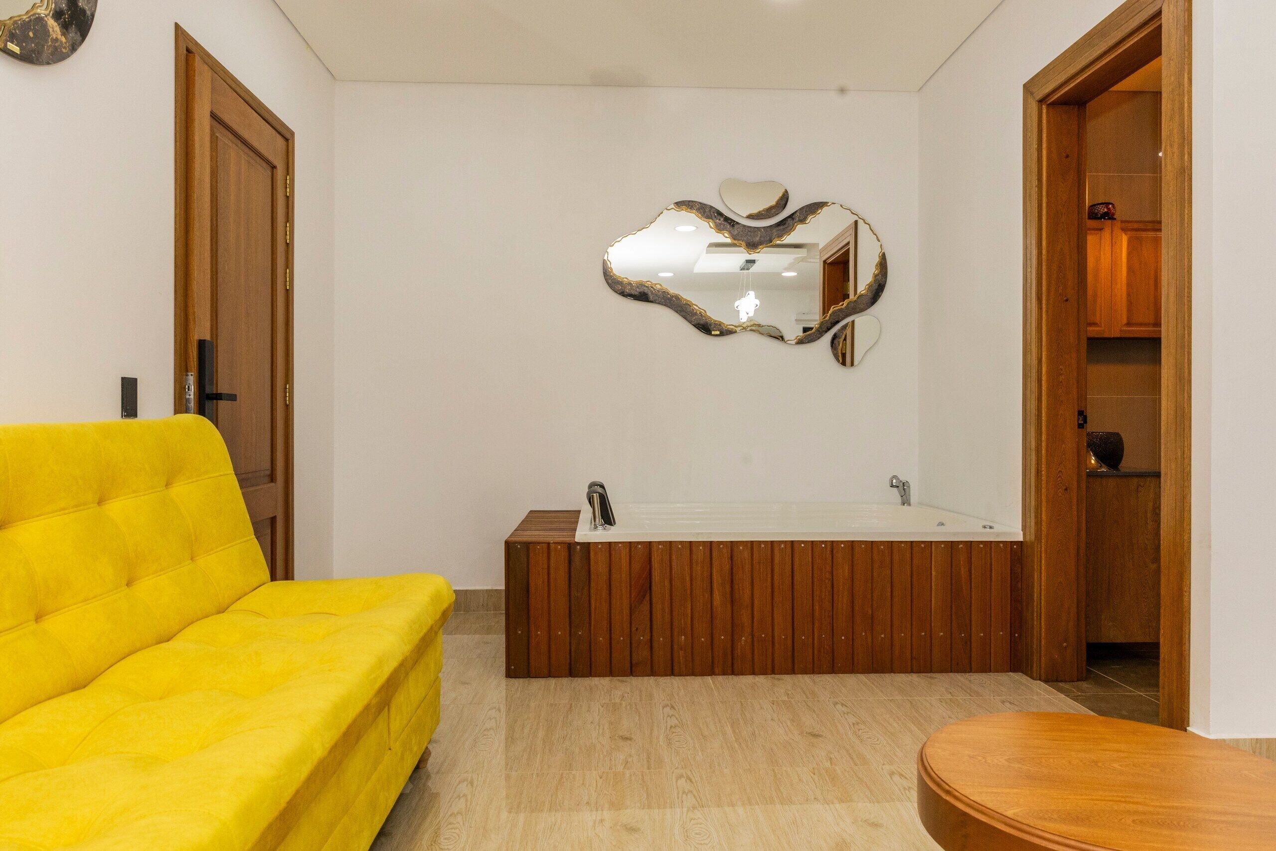Un baño con una bañera de madera, un sofá amarillo y un espejo con marco en forma de corazón.