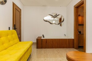 Une salle de bain avec une baignoire en bois, un canapé jaune et un miroir dont le cadre est en forme de cœur.