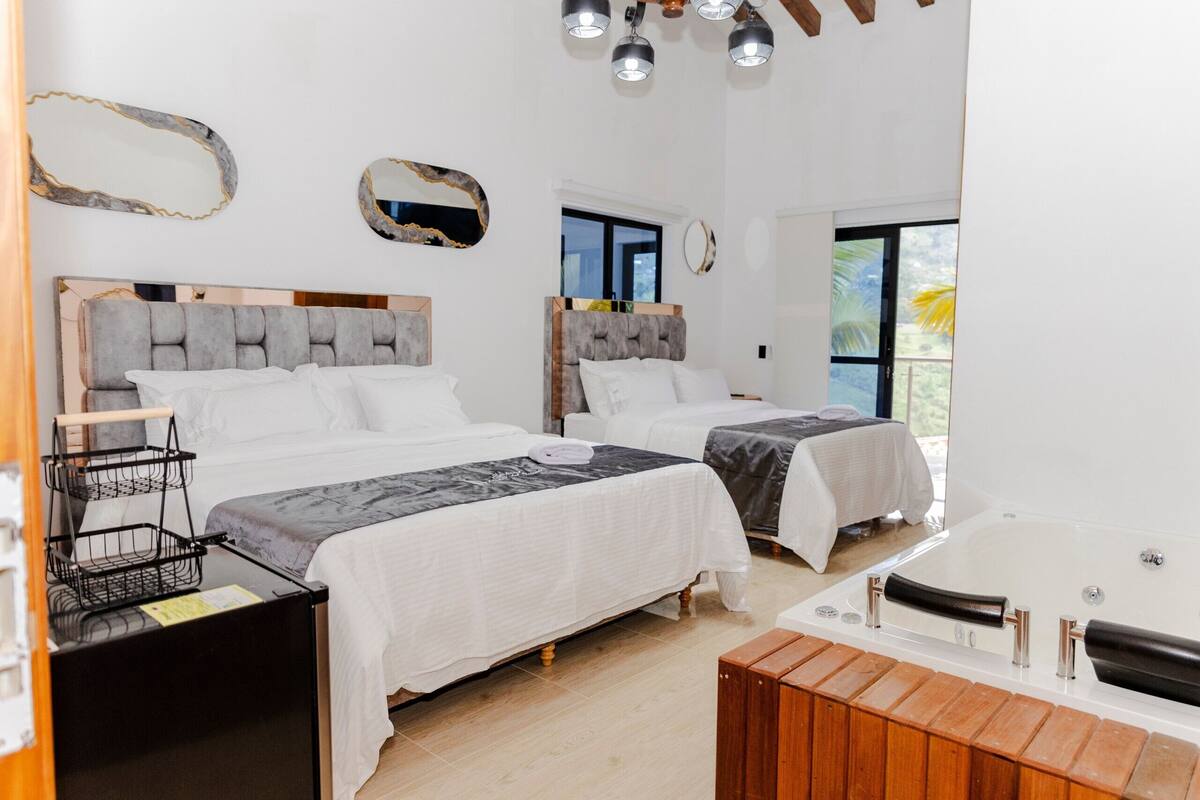 Een hotelkamer met twee bedden, een houten bankje, een badkuip en een grote spiegel.