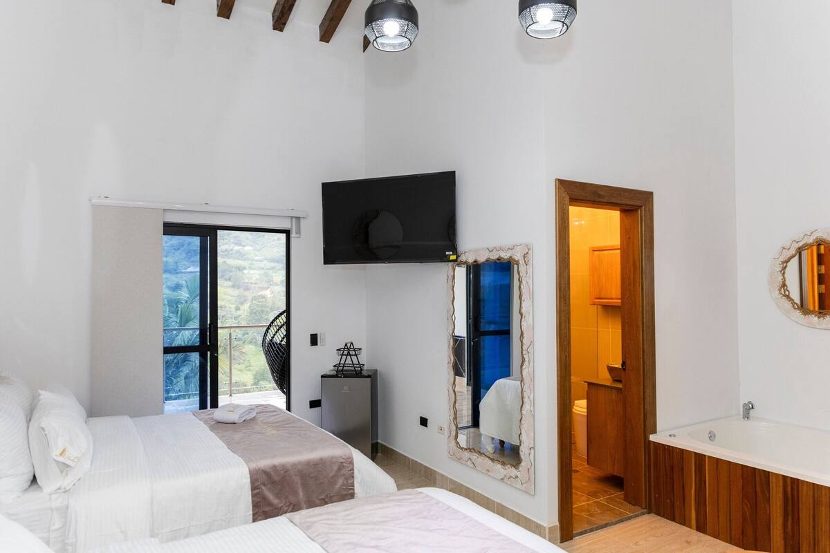 Een slaapkamer met een bed, een televisie, een spiegel en een deur naar de badkamer.