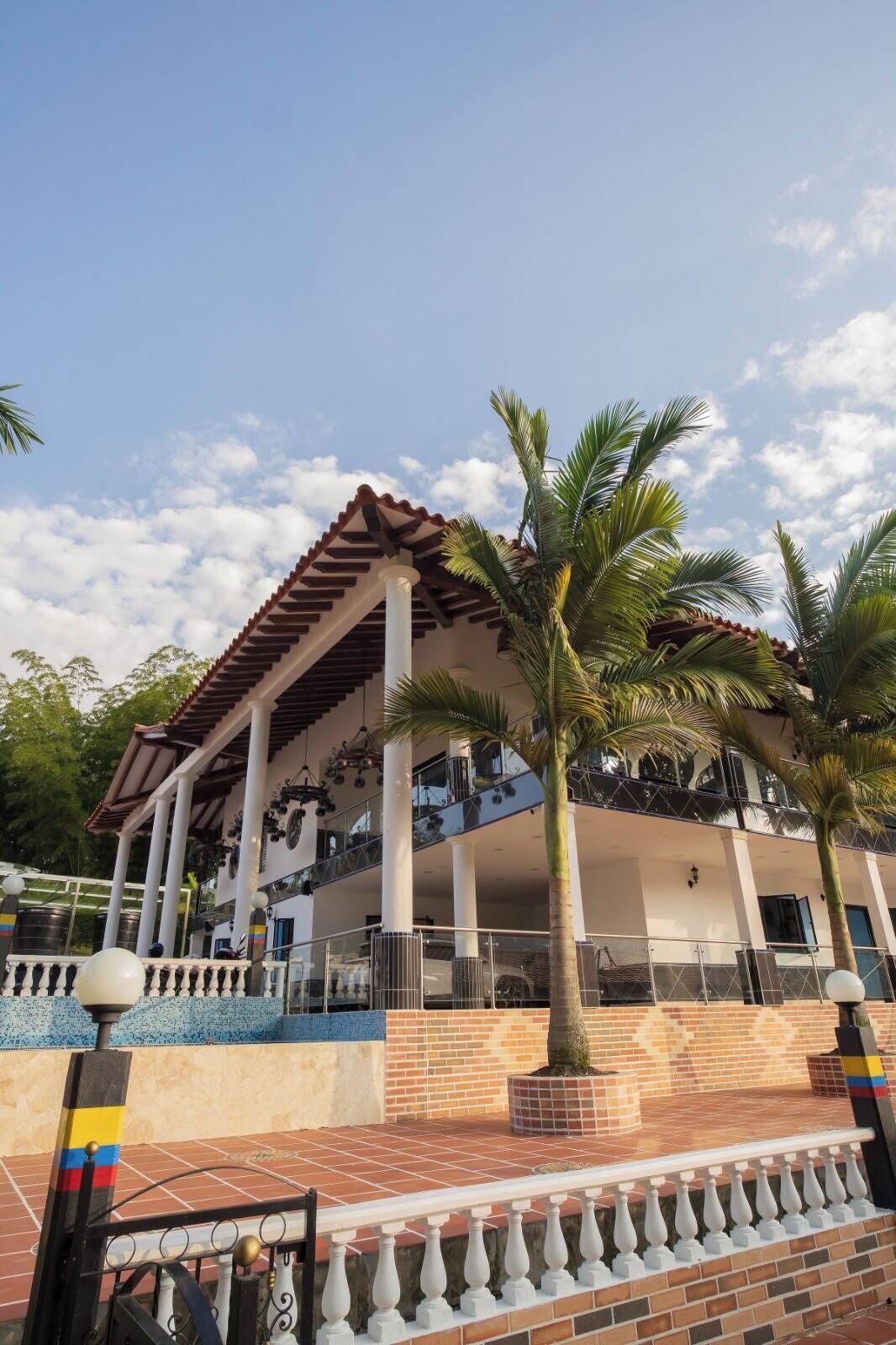 Un hotel con un área exterior techada, palmeras y un patio con baldosas.