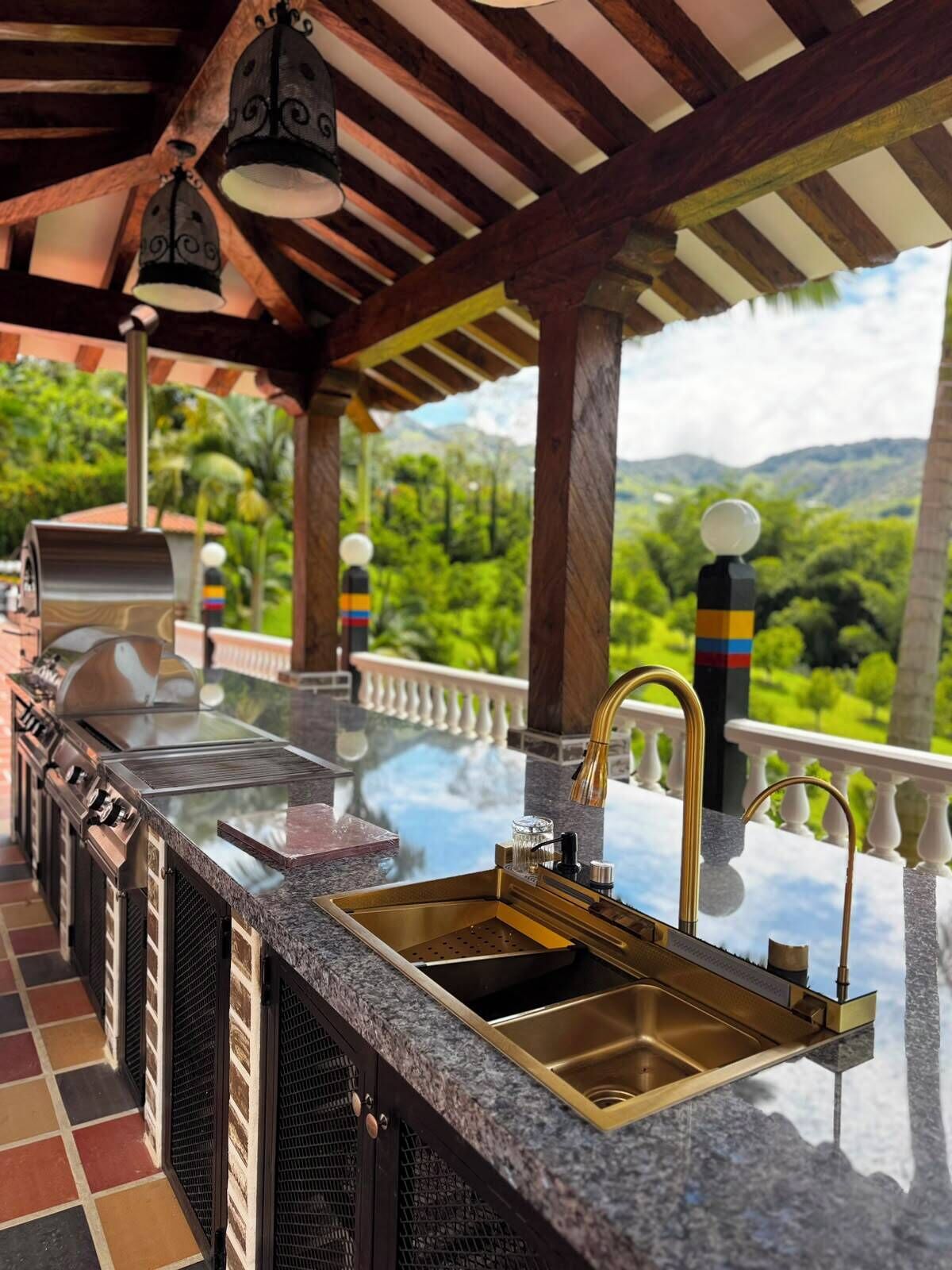 Cocina exterior con una parrilla, un lavamanos y vistas a un paisaje exuberante.