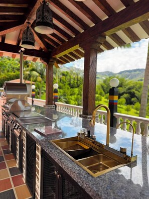 An outdoor kitchen with a grill, a sink, and a view of a lush landscape. - Ecohotel Dubai Del Oriente (El Penol)