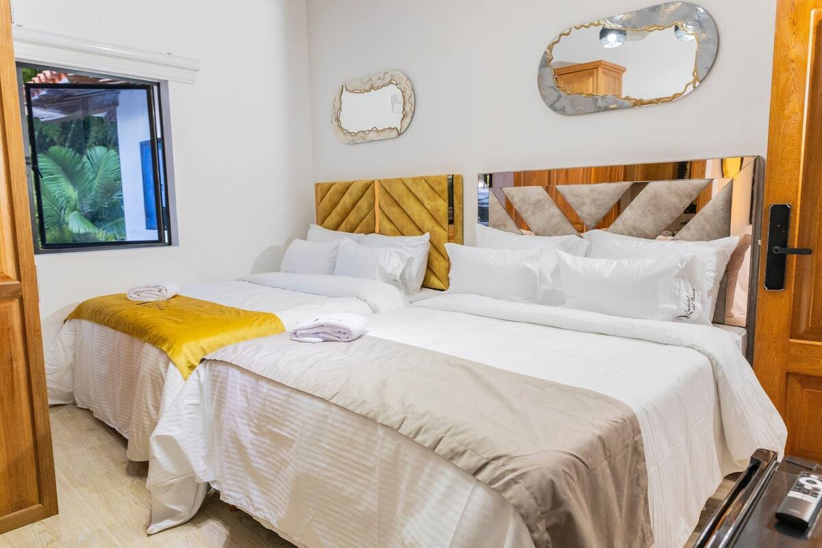 Een tweepersoonsbed met een houten hoofdeinde, witte beddengoed en een gele plaid.