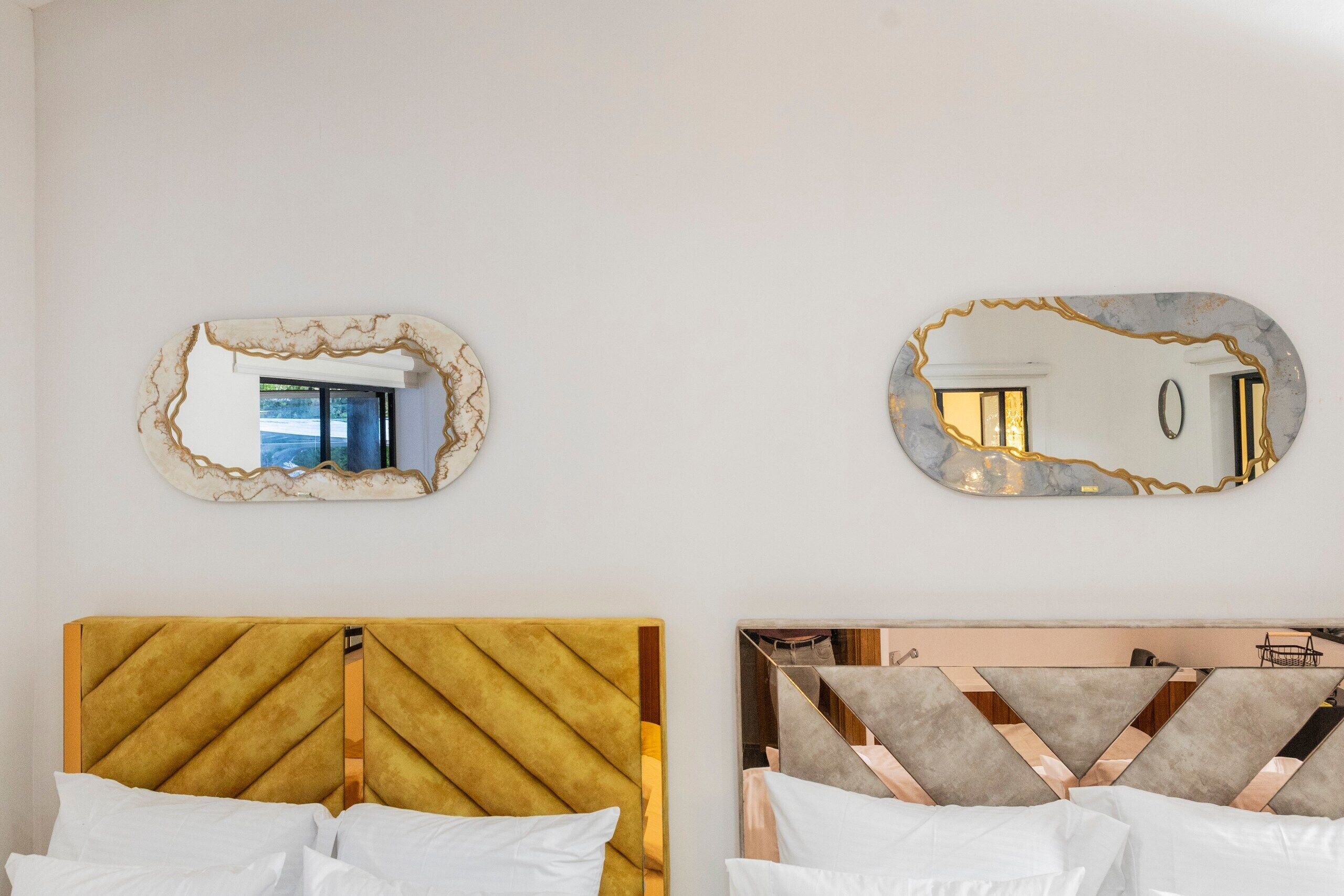 Two beds with distinct headboards, a wall-mounted mirror, and a window with a view.
