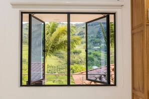 A room with a large window offering a view of a lush green landscape and a palm tree. - Ecohotel Dubai Del Oriente (El Penol)