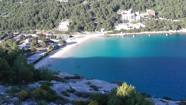 Eine Küstenansicht mit Strand, felsigem Gelände und Gebäuden im Hintergrund.