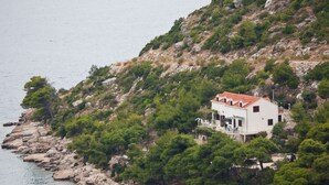 Ein Küstenhaus mit rotem Ziegeldach, umgeben von viel Grün und felsigem Gelände.