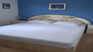 Ein Bett mit Holz-Kopfteil, ein Nachttisch mit Lampe und ein gerahmtes Bild an der Wand.