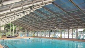 Een binnenzwembad met overdekt dak, helder zwembadwater en een zonnedek met stoelen.