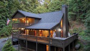 Een chalet met twee verdiepingen, een balkon, een schoorsteen en lichtslingers.