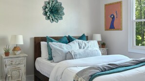 Ein Schlafzimmer mit einem Bett, einem Deckenventilator, einer Wanddekoration, einem Fenster und einem Nachttisch mit Lampe.