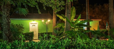 Un edificio con fachada verde, puerta blanca y un poste de luz iluminado.
