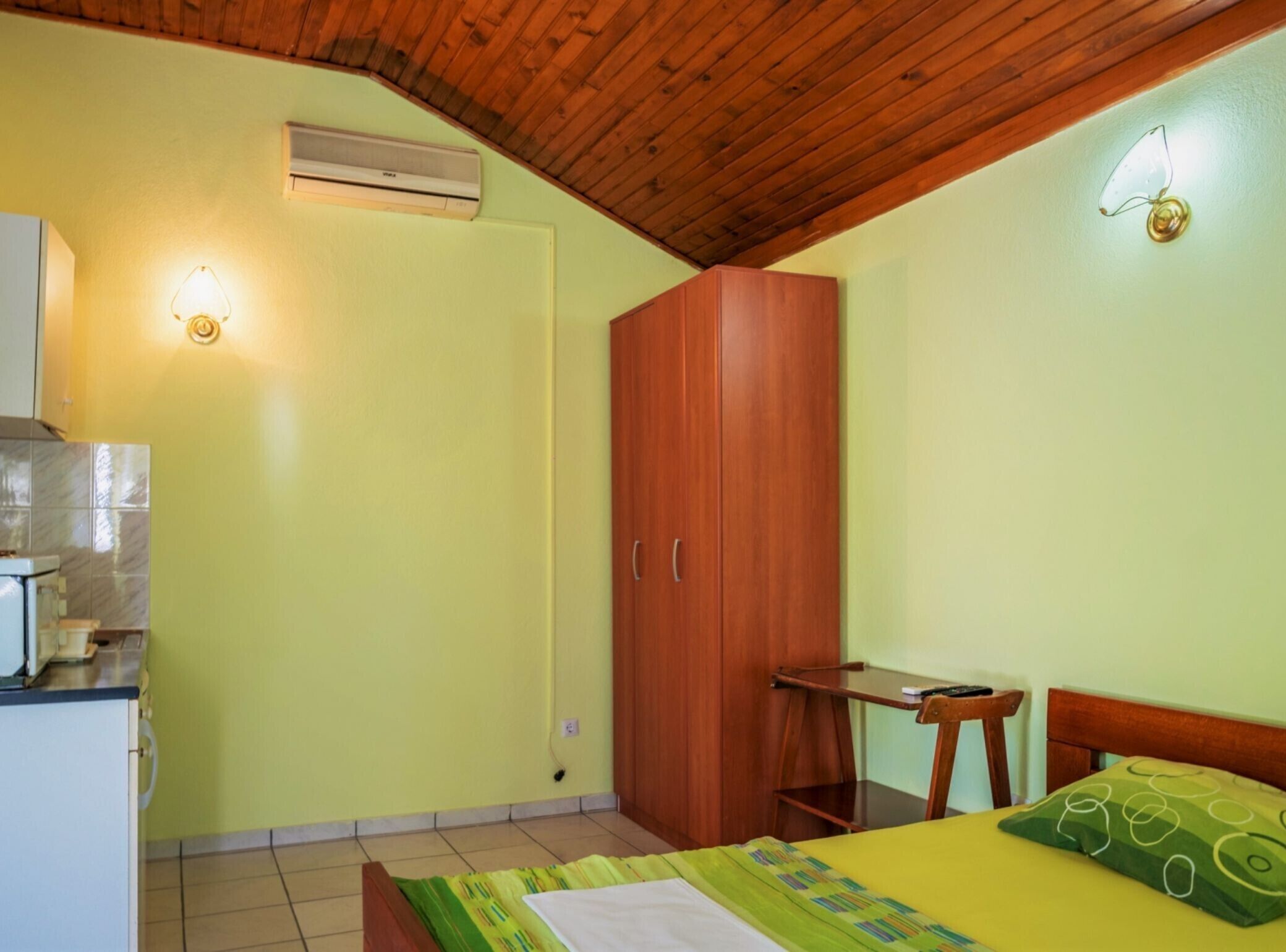A room with a bed, a wooden wardrobe, a desk, and a wall-mounted air conditioner.