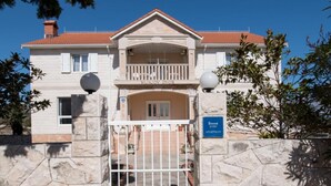 Un edificio de dos pisos con fachada de piedra, entrada con reja y un balcón.