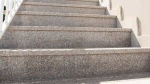 Unos escalones de granito con barandilla blanca.