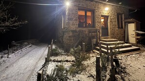 Una casa in pietra con ingresso illuminato, una recinzione in legno e terreno coperto di neve.