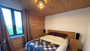 Una camera da letto con soffitto in legno, un'ampia finestra, un letto con coprialetto, comodini e una lampada.