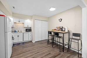 Cocina compacta con gabinetes blancos, un microondas y una cafetera sobre una mesita.