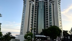 Een modern hoog gebouw met een gebogen glazen gevel, meerdere balkons en een bord met de tekst 'Tropical Executive'.