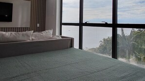 Een moderne slaapkamer met een groot bed, een aan de muur bevestigde televisie en uitzicht op de lucht door grote ramen.