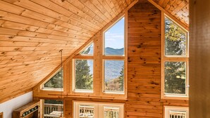 Eine Holzhütte mit geneigtem Dach, mehreren Fenstern und Blick auf eine bewaldete Berglandschaft.
