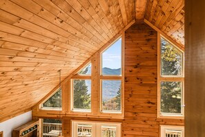 Eine Holzhütte mit geneigtem Dach, mehreren Fenstern und Blick auf eine bewaldete Berglandschaft.