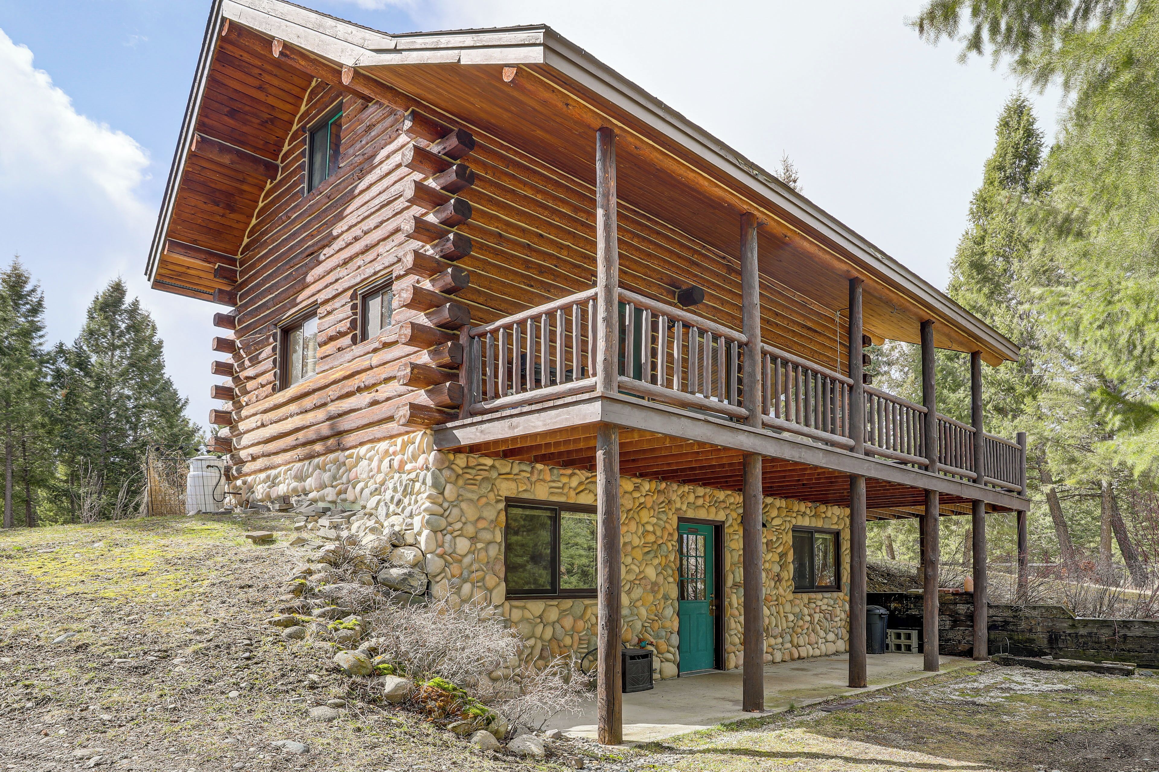 A log cabin with a stone foundation, a balcony, and a door.