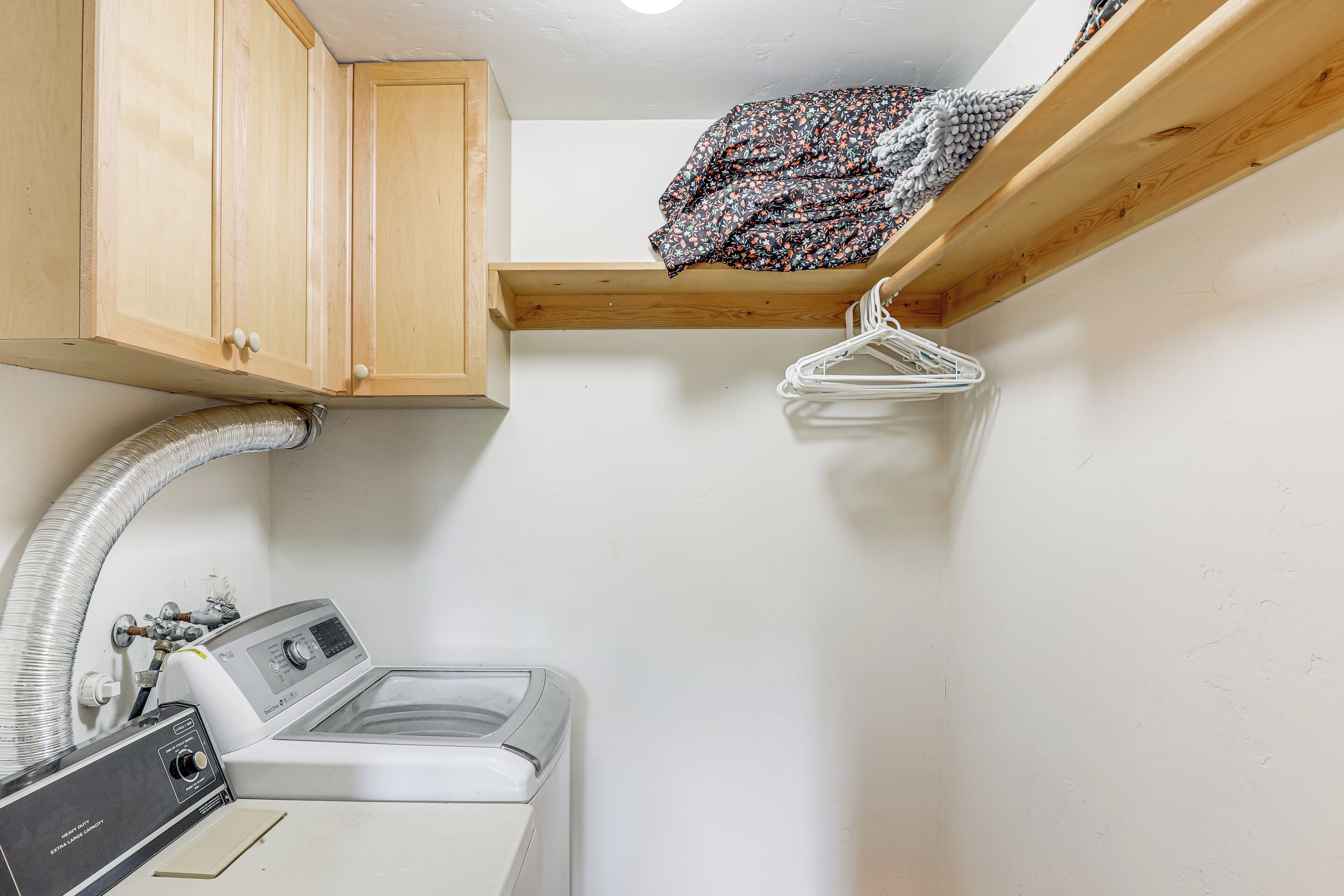 A compact laundry room with a washing machine, wooden cabinets, and a clothes drying rack.