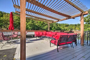 Una terraza de madera con muebles de exterior rojos, incluyendo un sofá y sillas, bajo una pérgola.