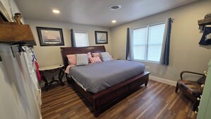 Une chambre à coucher avec un lit en bois, une table de chevet, une commode et une fenêtre avec des rideaux.