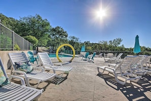 Zona junto a la piscina con sillones de descanso, un arco decorativo amarillo y cielo azul despejado.