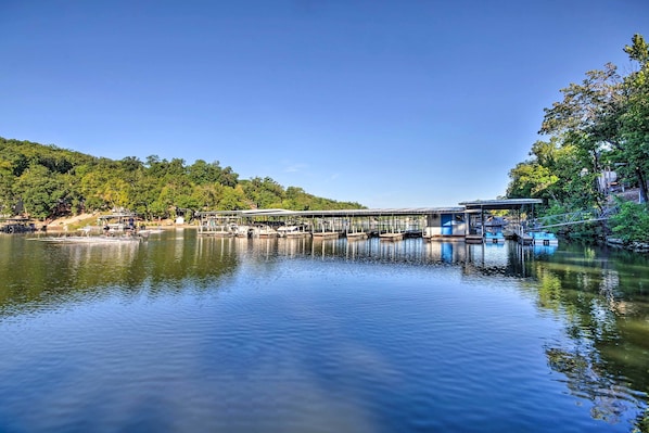 Un lago tranquilo con un muelle y barcos, rodeado de árboles y colinas.