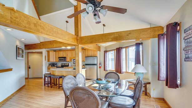 A spacious dining area with a glass table and wicker chairs, a kitchen in the background, and a ceiling fan.