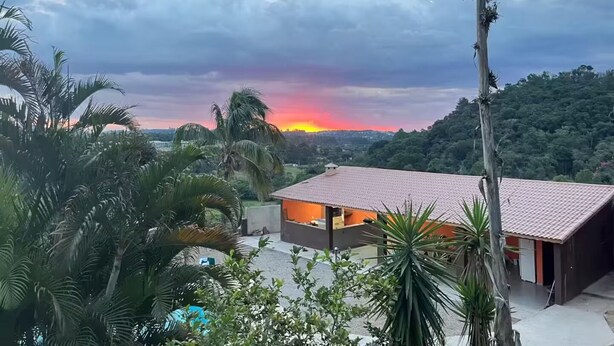 Una casa de techo rojo, rodeada de vegetación, con un atardecer al fondo.