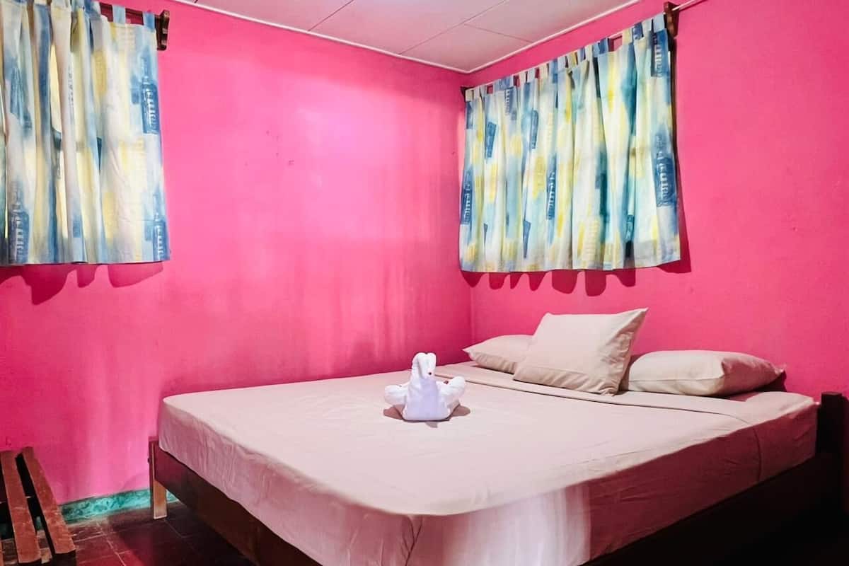 A room with a bed, pillows, curtains, and a wooden chair.