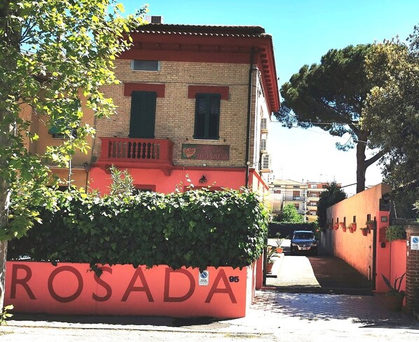 A building with a red facade, a visible sign reading 'CASA ROSADA,' and a large planter with the text 'ROSADA' in the foreground.
