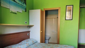 A room with a bed, a wooden headboard, a green wall, a white cabinet, a toilet, and a shower door. - PortoRecanati Zimmer (Porto Recanati)