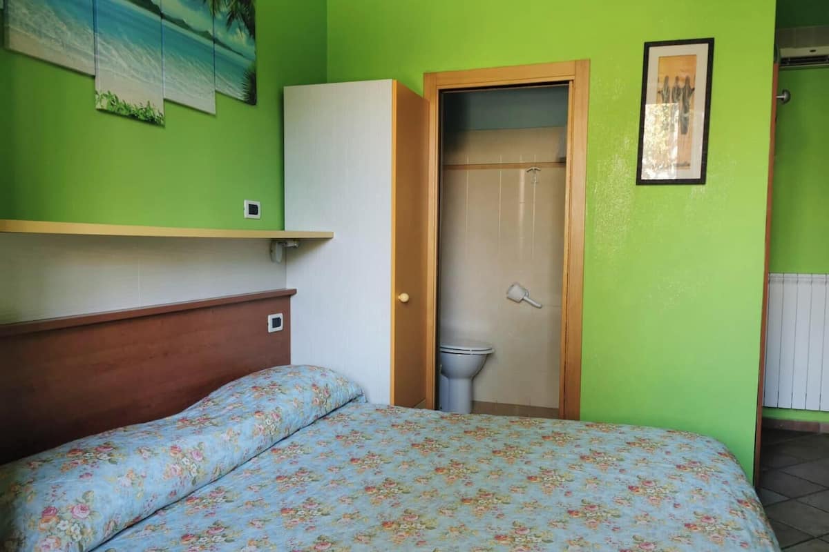 A room with a bed, a wooden headboard, a green wall, a white cabinet, a toilet, and a shower door.