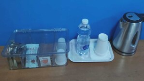 A clear plastic storage box with compartments, a water bottle, a white cup, and a stainless steel kettle on a table. - PortoRecanati Zimmer (Porto Recanati)