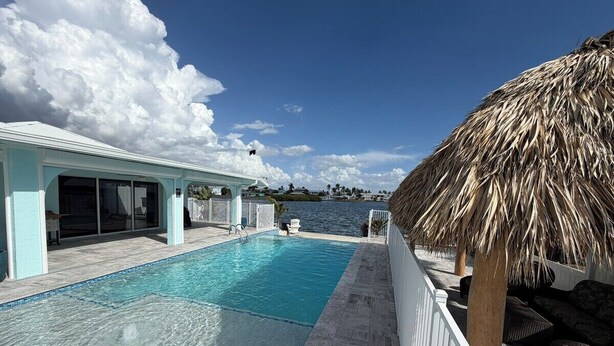 A swimming pool with a clear blue water, a thatched roof, and a view of the sea. - Waterfront Matlacha views! 2/2 Heated Pool Home (Matlacha)