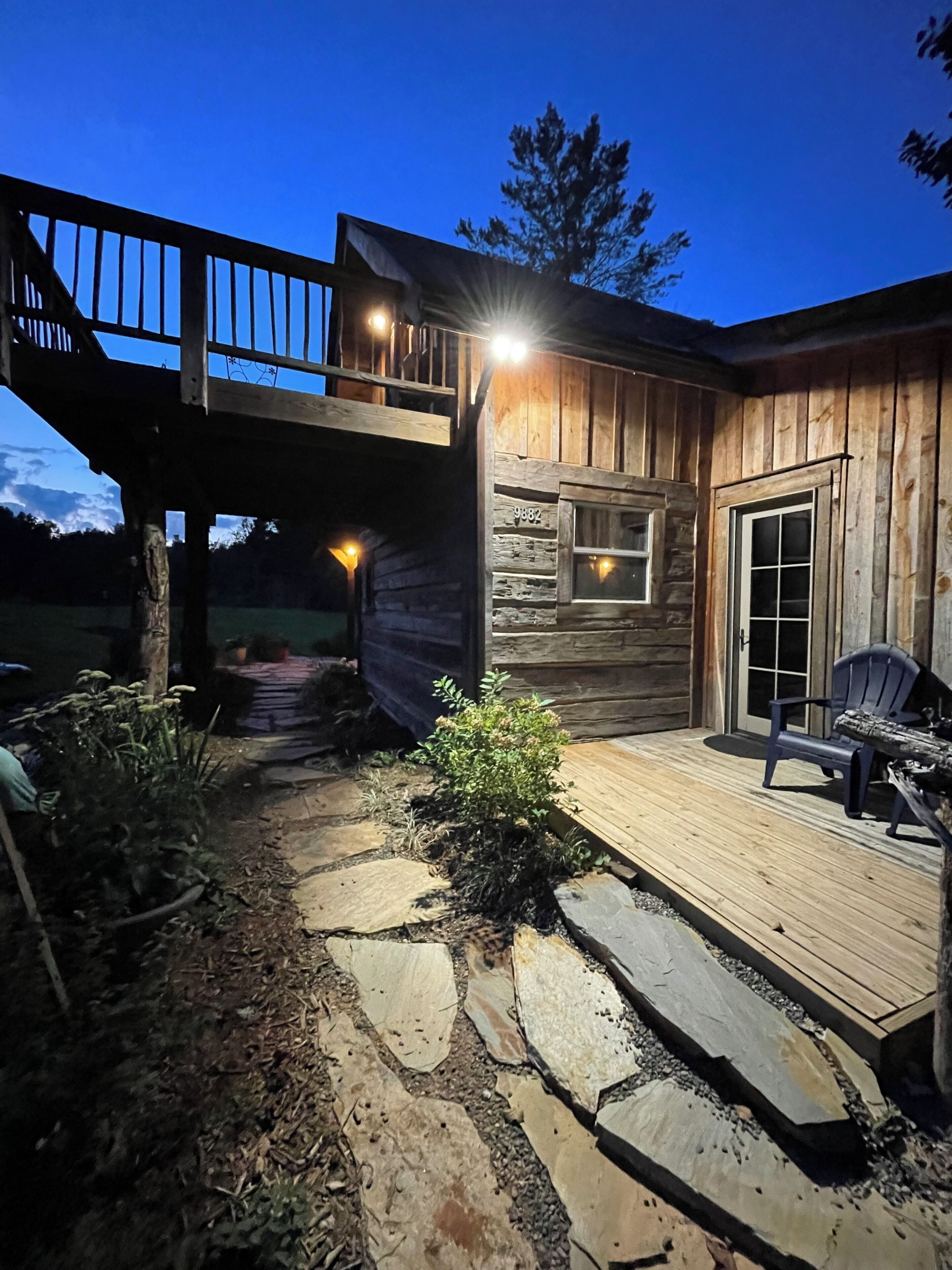 A wooden cabin with a stone pathway leading to a deck, a balcony, and a door with a window.