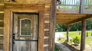 Uma cabana de madeira com uma porta grande, varanda coberta e um vaso com planta.