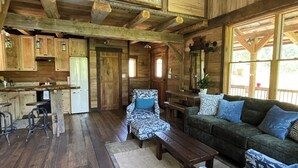 Interior espaçoso de cabana com teto alto, vigas de madeira, área de jantar, conjunto de sofás e cozinha.
