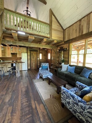 Geräumiges Cabin-Interieur mit hoher Decke, Holzbalken, einem Essbereich, einer Sofagruppe und einer Küche.